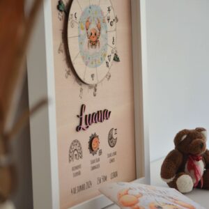 Quadro de mapa astrológico infantil em madeira da Pinóquio Woodart com o nome Luana e o livro de interpretação "O Teu Céu Interior" ao lado.