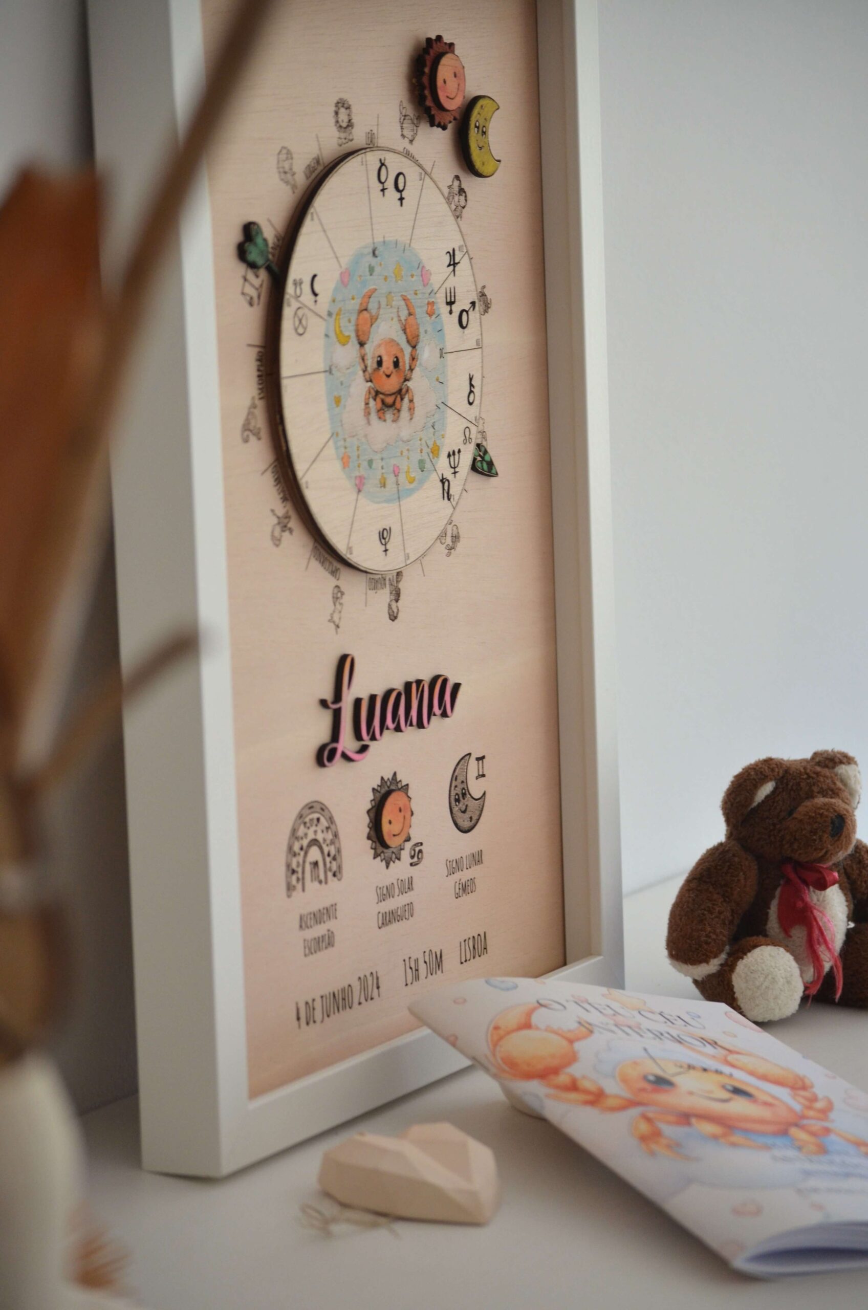 Quadro de mapa astrológico infantil em madeira da Pinóquio Woodart com o nome Luana e o livro de interpretação "O Teu Céu Interior" ao lado.